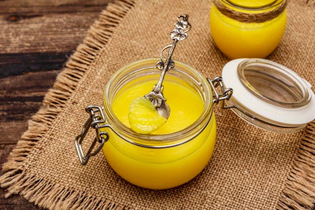 Pure Or Desi Ghee (Ghi), Clarified Melted Butter. Healthy Fats Bulletproof Diet Concept Or Paleo Style Plan. Glass Jars, Silver Spoon On Vintage Sackcloth. Wooden Boards Background, Close Up Pure Desi Ghee