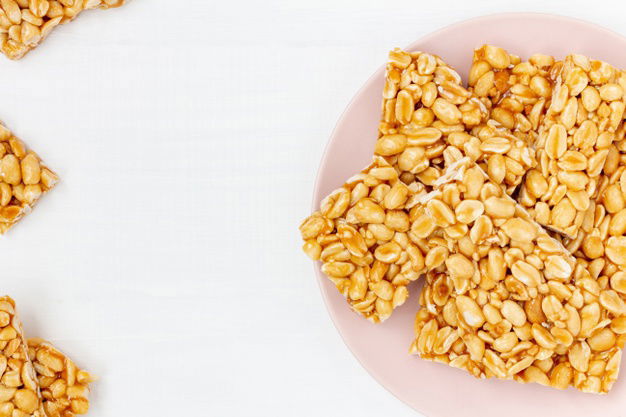 Top 5 Fascinating Health Benefits Of Kadalai Mittai! 5 Plate Peanut Brittle Candy Pieces White Wooden Background Top View Copy Space 158417 219 1