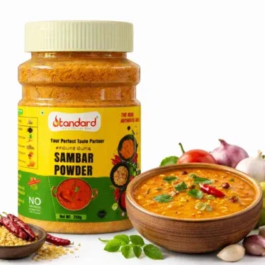 Standard Sambar Powder 250g jar with freshly prepared South Indian sambar in a bowl and spices on white background.